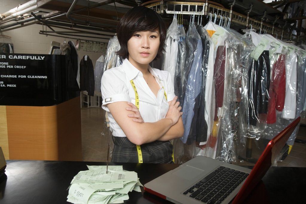 Confident Woman With Receipt Spike And Laptop On Counter In Laundry