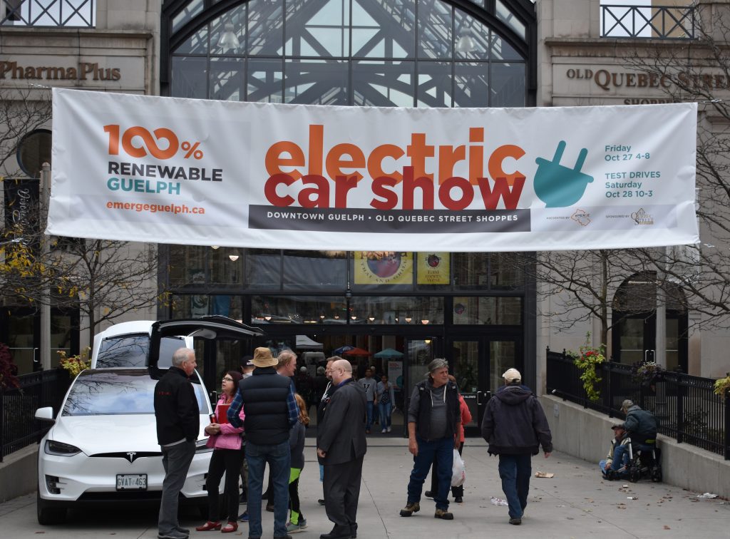 The front of Old Quebec Street Shoppes, Guelph, with a large electric car show banner and a crowd of people