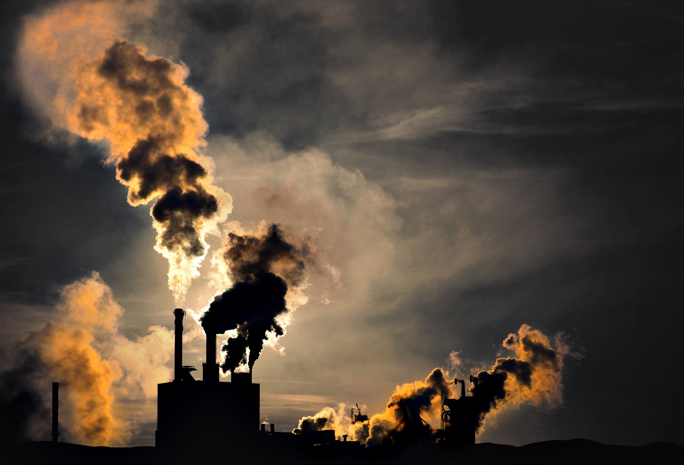 Silhouette of factory with chimneys and heavy smoke