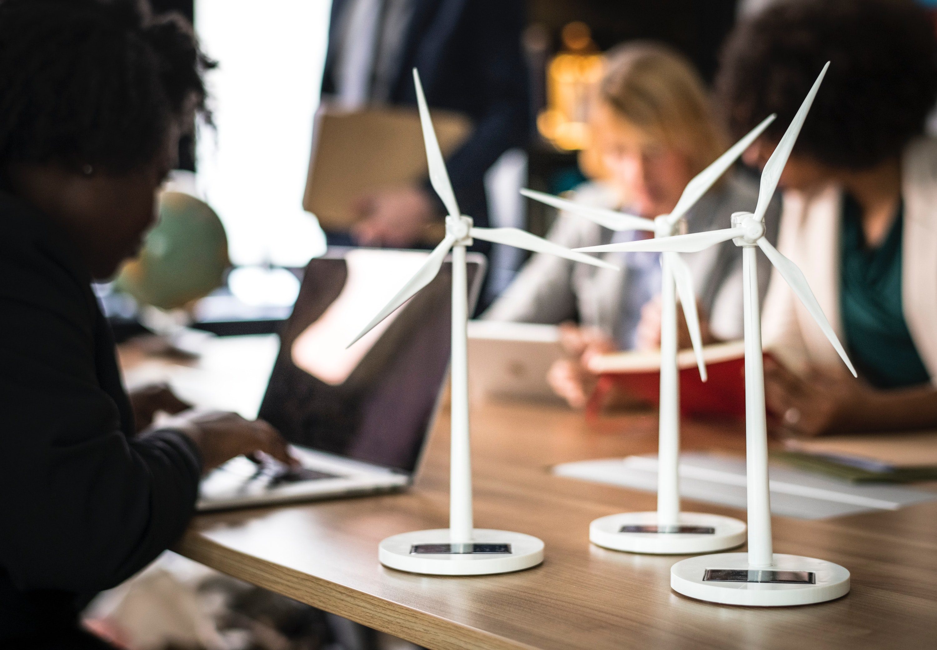 An image of small mock-ups of windmills on a boardroom table. People with computers are working in the background.