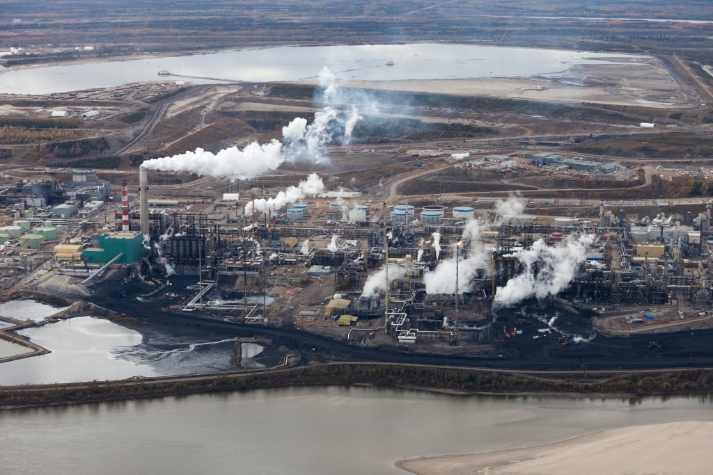 Aerial view of A large oil refinery along the Athabasca River in Alberta's Oilsands, showing multiple smoke stacks.