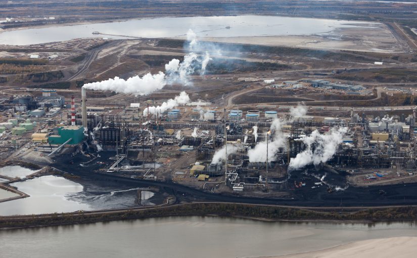 Aerial view of A large oil refinery along the Athabasca River in Alberta's Oilsands, showing multiple smoke stacks.