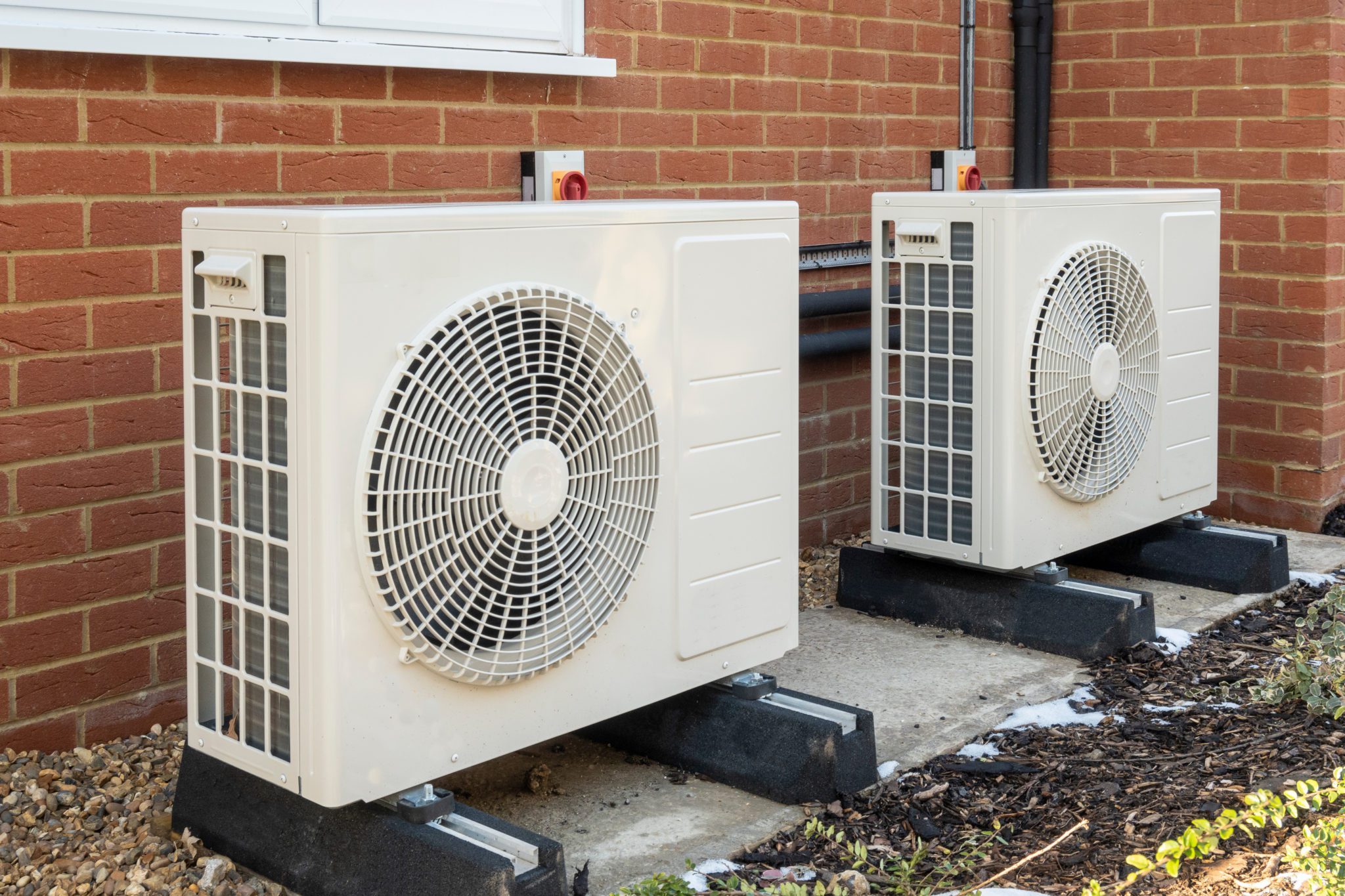 Two heat pumps installed outside a brick house