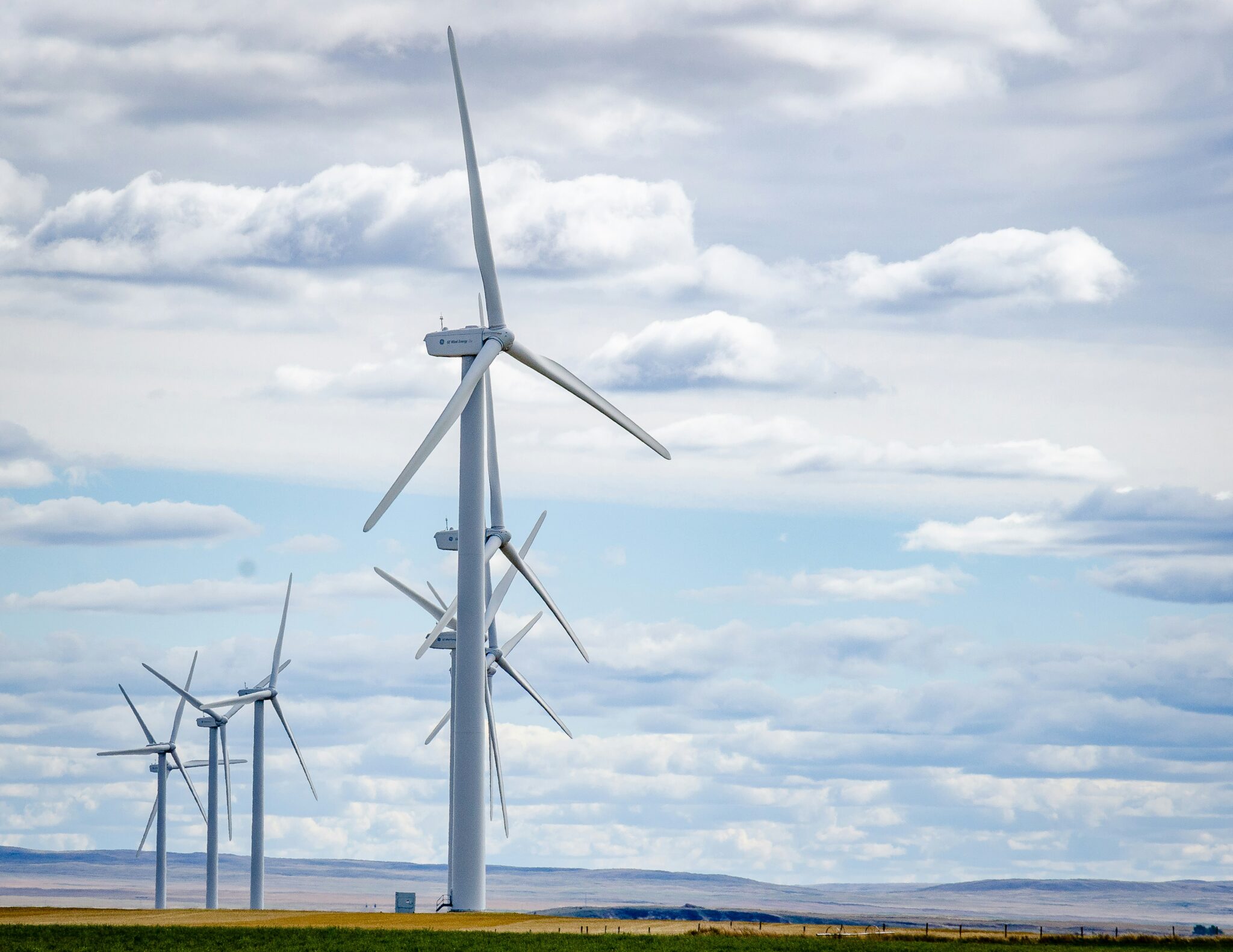 A series of wind turbines in a field with a gray cloudy sky.