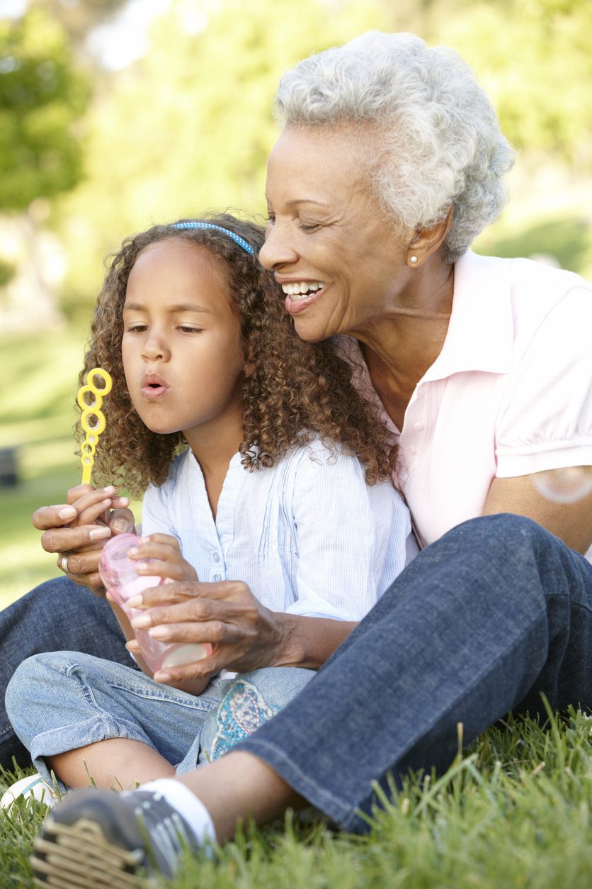 Grandmother And Granddaughter Blowing Bubbles In Park