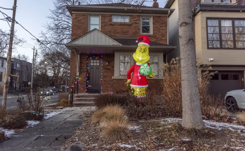 The grinch outside a home decorated for Christmas