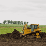 Bulldozer digging up land in front of a farm