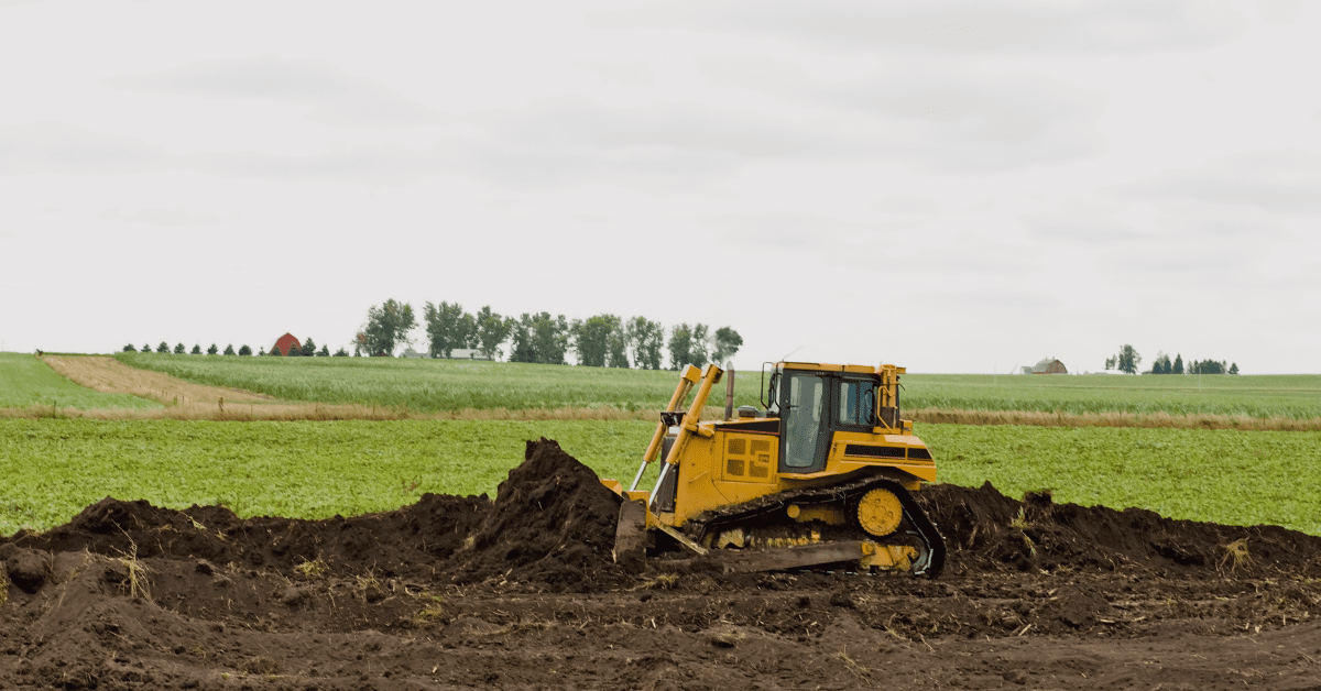 Bulldozer digging up land in front of a farm